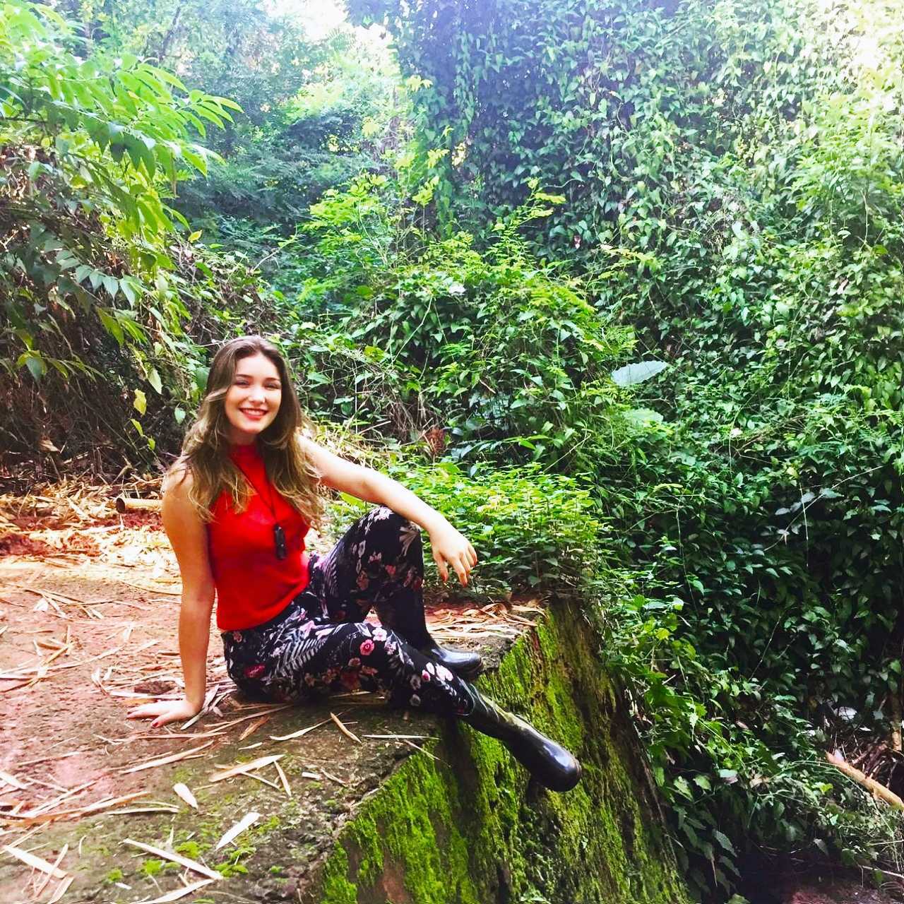 Ana Paula Andreazzi smiling, sitting on a moss-covered wall beside a forest trail
